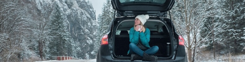 Image of snowy road with woman sipping coffee in the back of the car.
