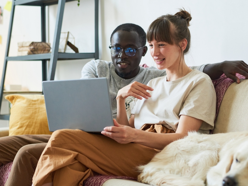A young interracial couple sitting on a couch looking at a laptop mobile