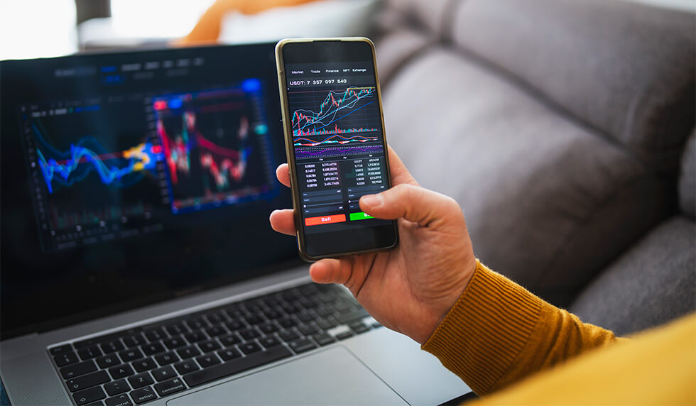 Close up of a laptop and a person's hand with a phone in it while both devices are displaying financial analysis charts