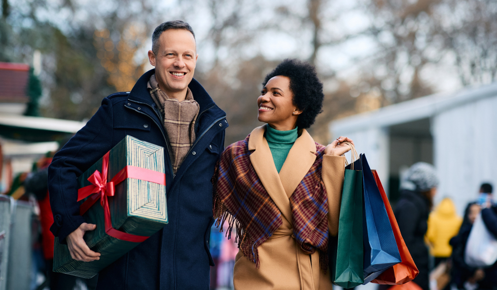 Happy white man with African American woman with holiday gifts walking through the city.